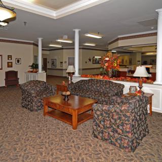 A cozy lobby area with sofas and chairs arranged around a wooden coffee table, complemented by warm lighting and decorative elements.