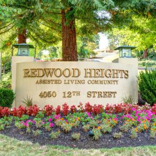 Entrance sign for Redwood Heights Assisted Living Community surrounded by flowers.