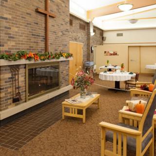 A cozy chapel interior featuring a brick fireplace, wooden seating area, and a cross on the wall.