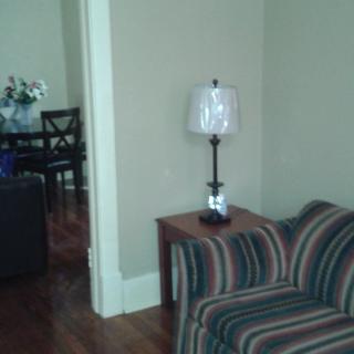 A cozy living room with a striped sofa, side table, and lamp, leading into a dining area.