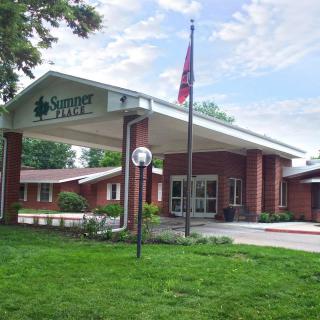 The exterior entrance of a nursing home with a flagpole and surrounding greenery.