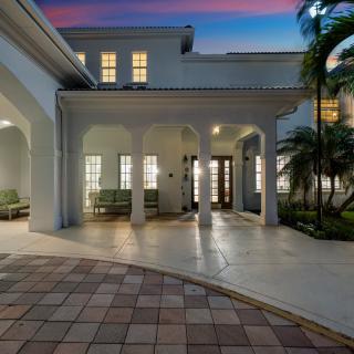 A beautifully lit house entrance with columns and a paved patio at dusk.