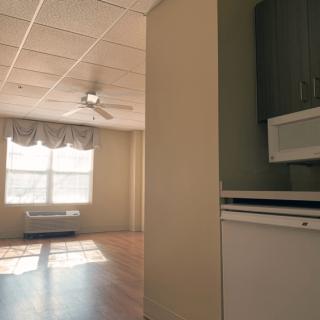 A cozy apartment interior featuring a living room and a kitchen area with ample sunlight streaming through the windows.