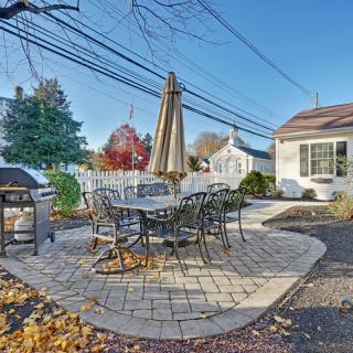 A cozy backyard patio with a table, chairs, and a grill set on brick pavers.