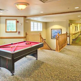 A cozy indoor game room with a pool table in a carpeted hallway featuring natural light from windows.