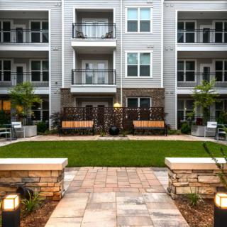 A modern apartment complex with a well-maintained courtyard featuring benches and greenery.