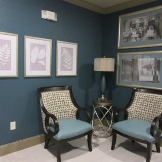 A cozy corner featuring two elegant chairs with blue cushions, a stylish lamp, and framed artwork on the blue walls.
