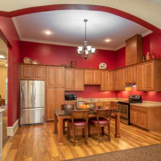 A cozy kitchen with wooden cabinets and red walls, featuring modern appliances and a dining table in the center.