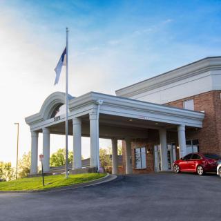 The front entrance of a hotel with a car parked outside and a flag displayed.