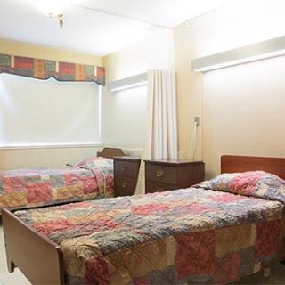 A simple hospital room featuring two twin beds with colorful bedding.