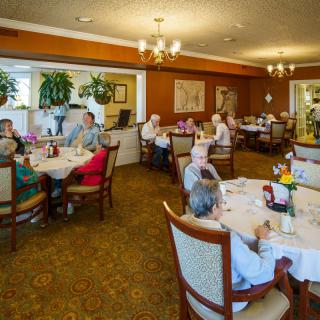 A group of elderly individuals gathered in a dining room, enjoying a meal together at various tables.