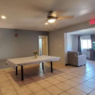 A modern living area featuring a covered table, sofa, and ceiling fan on a tiled floor.