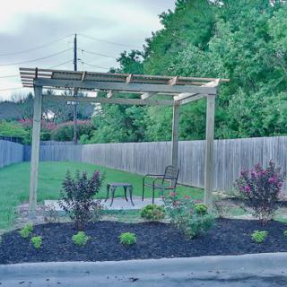 A peaceful garden area with a wooden pergola and neatly arranged plants.