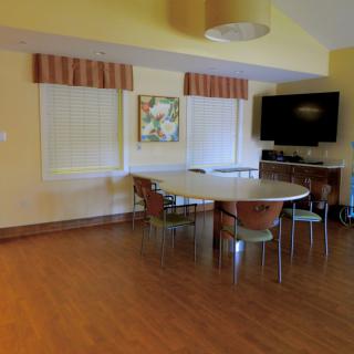 A cozy dining room with a round table and chairs, featuring a television and wooden flooring.