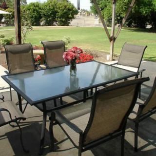 A patio setup featuring a glass table surrounded by six chairs, set in a garden.