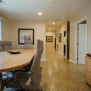 A well-lit conference room with a large meeting table and chairs, featuring artwork on the walls and an adjoining hallway.