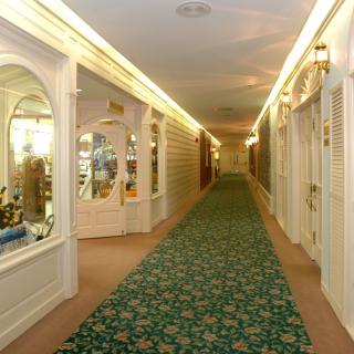 A well-lit hallway with a patterned carpet, showcasing decorative lighting and shopfronts on the sides.