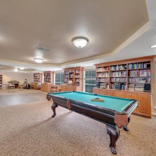 A spacious game room featuring a billiard table surrounded by bookshelves and cozy seating areas.