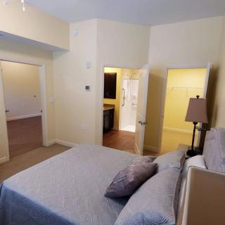 A cozy bedroom with a neatly made bed, neutral color palette, and multiple doorways leading to adjoining rooms.