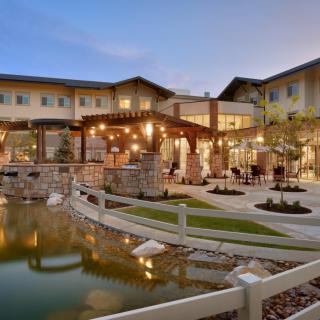 A beautifully lit building with an outdoor seating area by a pond at dusk.
