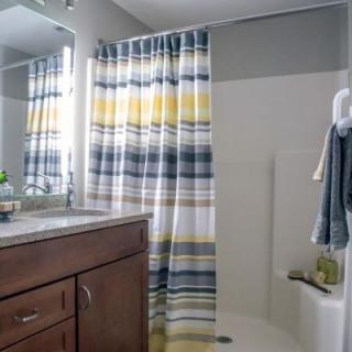 A modern bathroom featuring a striped shower curtain and a wooden cabinet with a mirror above the sink.