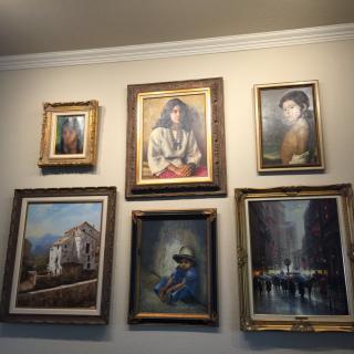 A collection of framed paintings displayed on a wall, featuring portraits and landscapes.