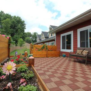 A cozy backyard patio with checkered decking, flower beds, and comfortable seating.