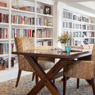 A cozy home library with bookshelves, a wooden table, and comfortable chairs.