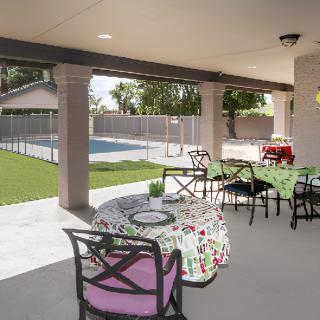 A covered patio with tables and chairs overlooking a garden and swimming pool.
