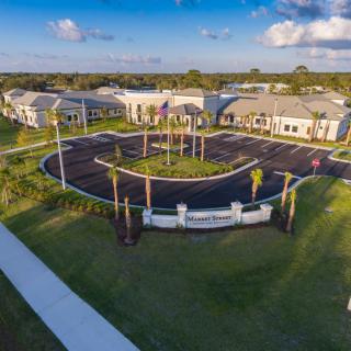 Aerial view of a modern building complex surrounded by lush greenery and palm trees under a partly cloudy sky.
