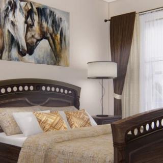A cozy bedroom featuring a wooden bed with decorative pillows, a painting of horses above, and a floor lamp by the window with elegant curtains.