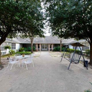 A cozy outdoor patio area with chairs and a swing set in front of a house surrounded by trees.