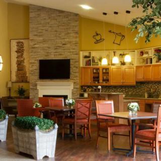A cozy living space featuring a dining area with orange chairs, a kitchen, and a fireplace, accented by greenery and warm lighting.
