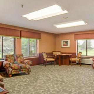 A cozy living room with large windows, comfortable seating, and a patterned carpet.