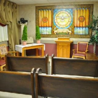 A small chapel interior featuring wooden pews, a stained glass window, and an altar.