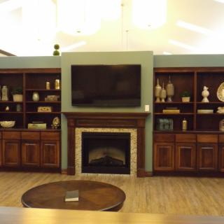 A cozy living room setup featuring a fireplace and television, surrounded by wooden shelves filled with decorative items.