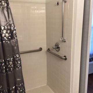 An accessible shower with grab bars and a patterned shower curtain.