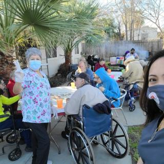 A group of people enjoying an outdoor gathering, with attendees in wheelchairs and wearing masks.