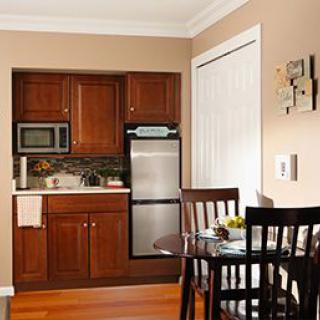 A cozy kitchen with wooden cabinets, featuring a mini fridge, microwave, and a small dining area.