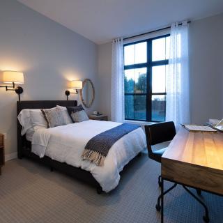 A cozy bedroom with a bed, desk, and large window.