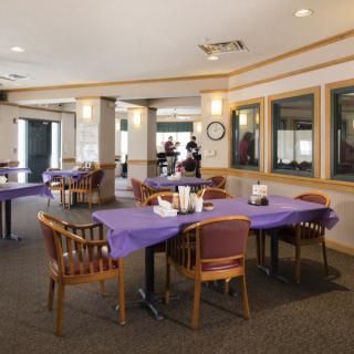 A spacious dining area with tables covered in purple tablecloths and wooden chairs.