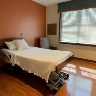 An empty hospital room with a bed and a window letting in natural light.