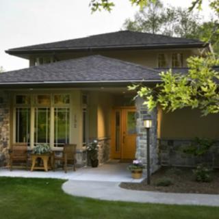 A modern residential house surrounded by a garden with trees and a porch.