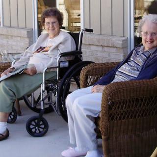 Two elderly individuals enjoying a relaxing time outdoors, one sitting in a wheelchair and the other in a wicker chair.