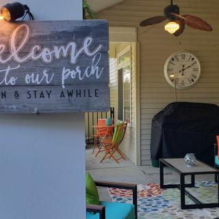 A cozy porch with welcoming decor, featuring a grill and vibrant patio furniture.