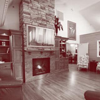 A cozy living room featuring a stone fireplace, hardwood floors, and various pieces of furniture and artwork.