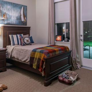 A cozy bedroom featuring a single bed with nautical-themed decor and a colorful blanket, next to a window with drawn curtains.