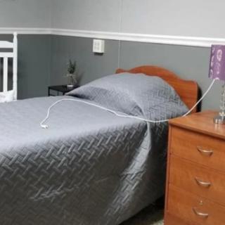 A hospital room featuring a single bed with grey bedding, an IV drip attached to the bedside, and a wooden nightstand.
