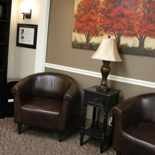 A cozy waiting area with two leather chairs, a lamp, and artwork on the wall.