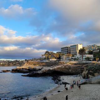 A picturesque view of a beachside landscape with rocky shores and modern buildings under a dramatic sky.